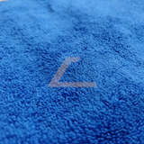A close-up of a bright blue textured fabric, likely a towel or blanket, featuring a large embroidered letter 'L' in a contrasting light color.