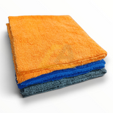 Three folded microfiber cleaning towels stacked on a white background, with an orange towel on top, followed by a blue towel, and a dark gray towel at the bottom.