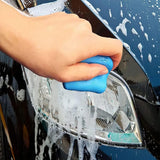 Hand using a blue sponge to clean the headlight of a black car.