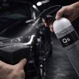 Person using a spray bottle labeled 'QS' to clean a car surface with a sponge.