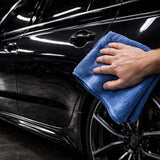 Person cleaning a black car with a blue microfiber towel