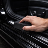 Hand using a black sponge to clean a car's interior surface.
