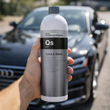 Hand holding a bottle of 'QS Quick & Shine' car care product with a blurred car in the background